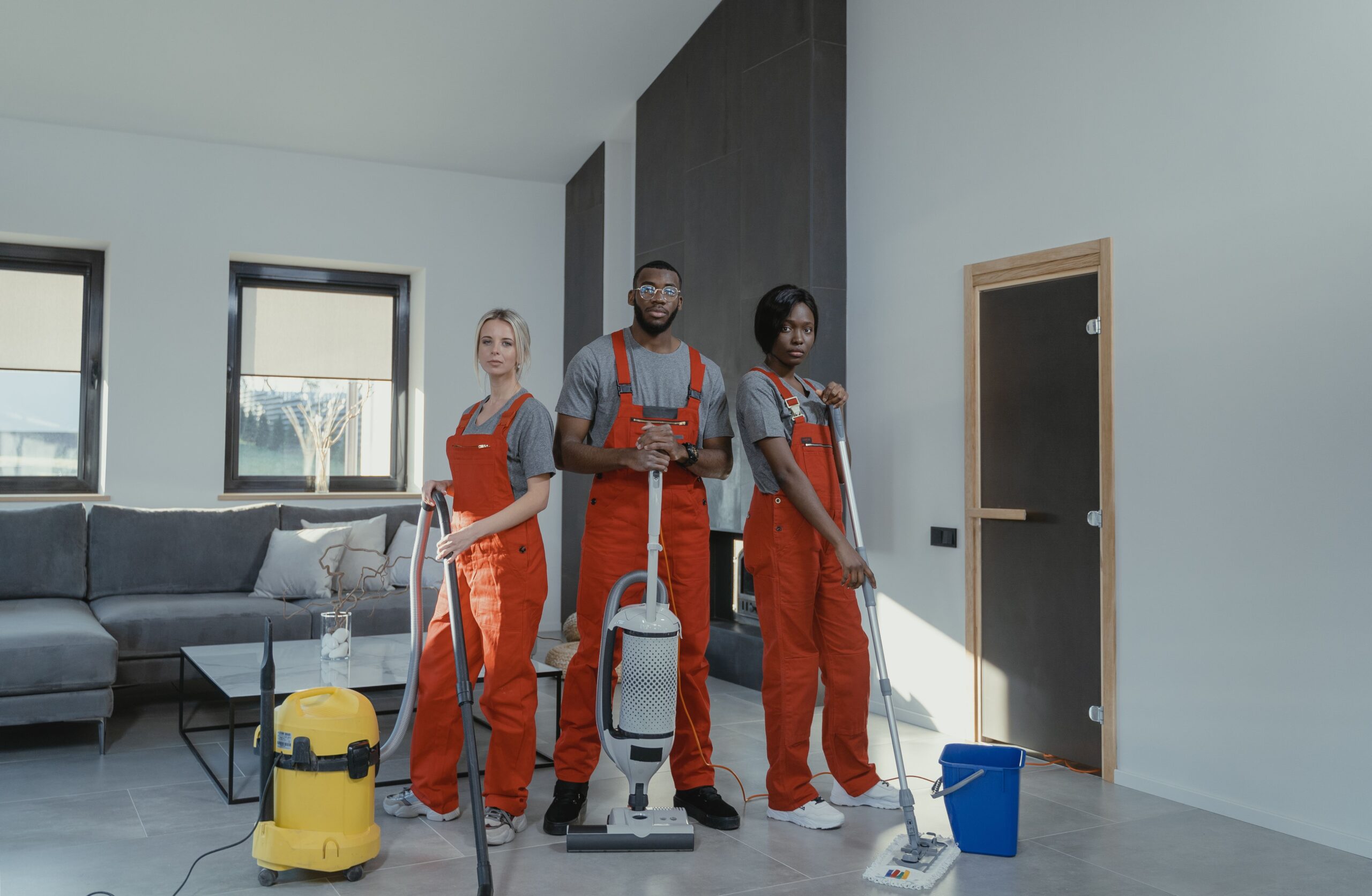My Guide to the Qualities of a Professional Cleaning Service Diverse cleaning team in red uniforms ready to sanitize a modern living room with vacuum and mop.