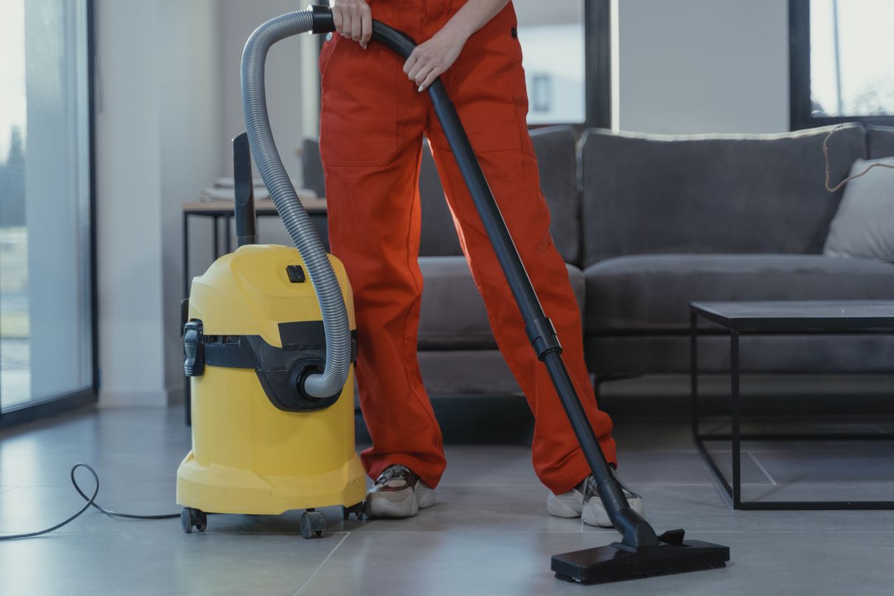 Home A professional cleaner in red coveralls vacuums a contemporary living room with a yellow vacuum cleaner.